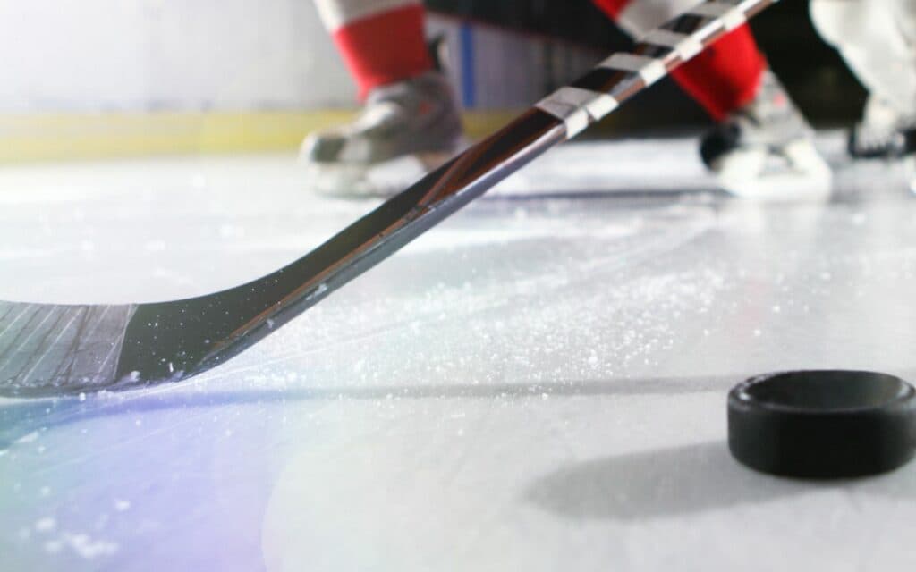 A hockey stick poised to strike a puck on the ice surface.