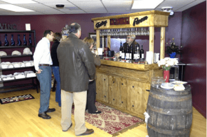 A group of people stands at a wooden bar counter in a wine tasting room.