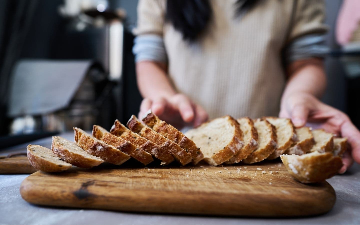 A person slices freshly baked bread on a wooden cutting board. A person slices freshly baked bread on a wooden cutting board.
