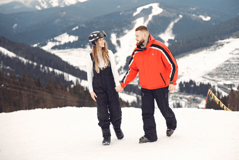 A woman and a man hold hands while walking on a snowy mountain slope.
