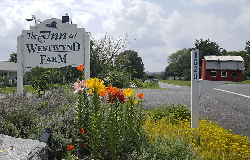Sign for The Inn at Westwynd Farm surrounded by flowers and a decorative mailbox.