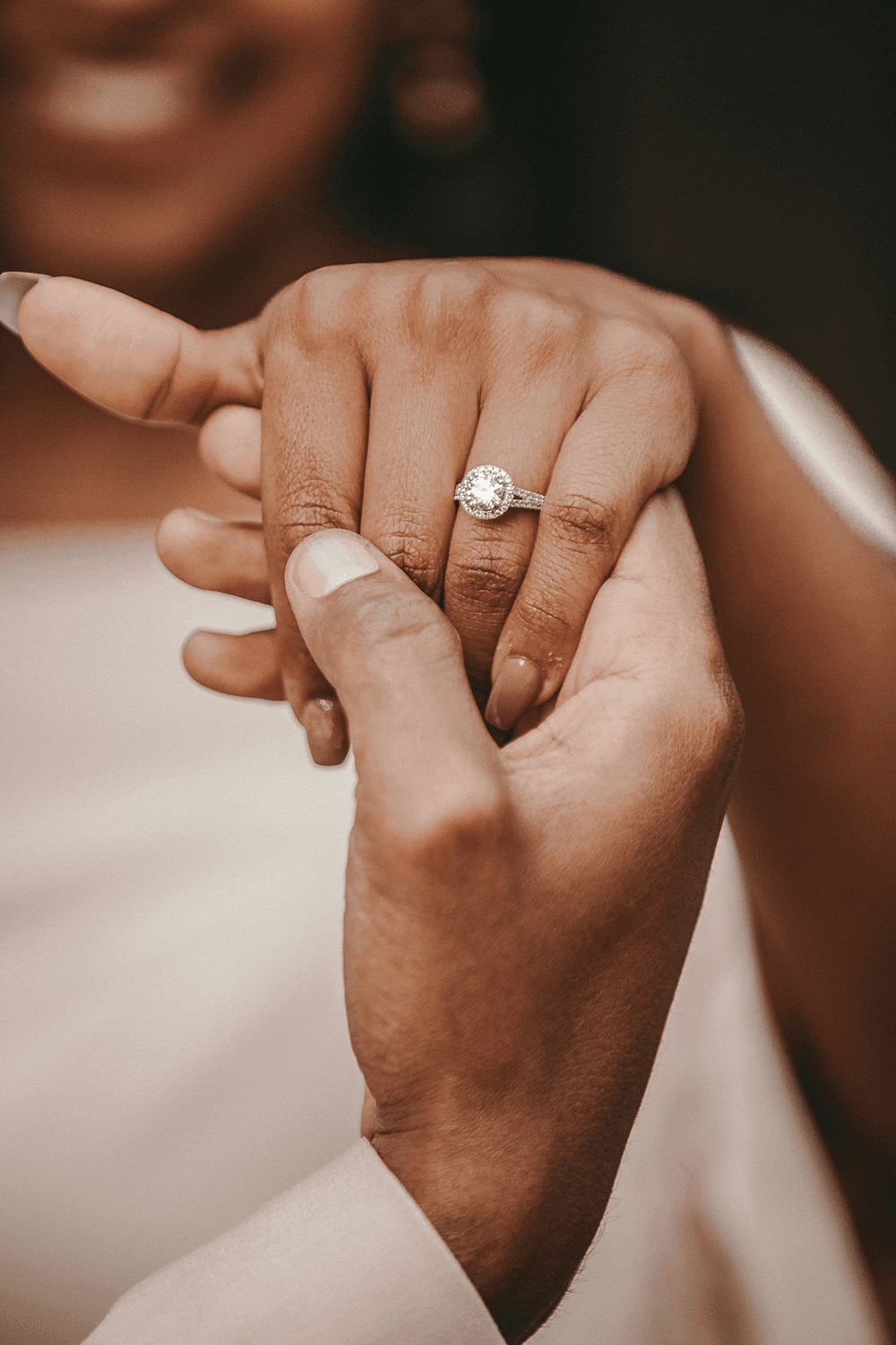 A close-up of two hands holding each other, showcasing an engagement ring on the woman's hand.
