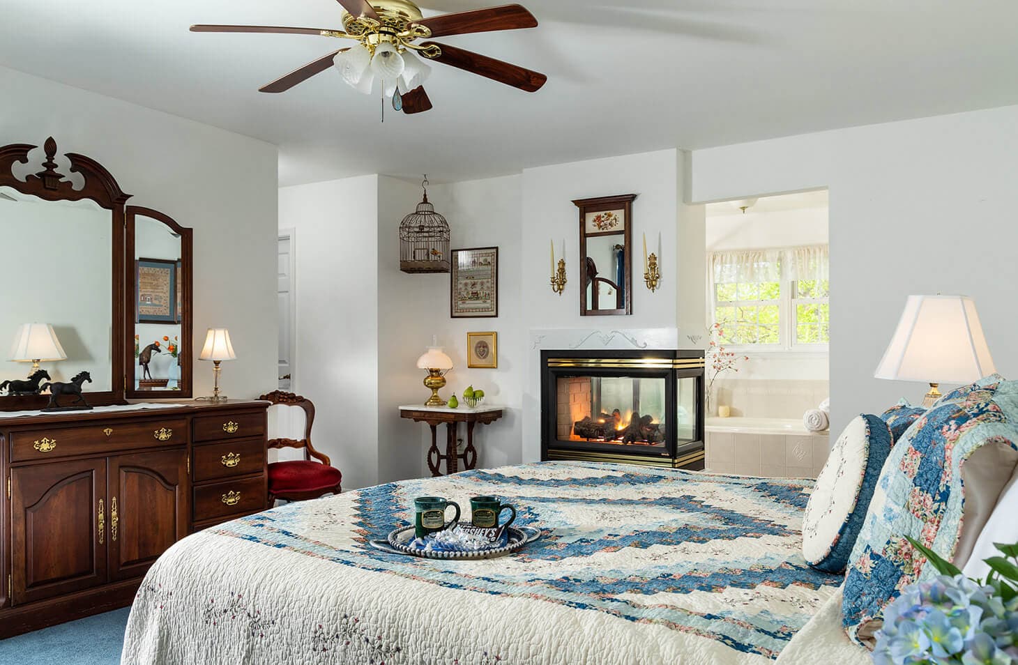 A cozy bedroom featuring a quilted bedspread, vintage furniture, and a stylish fireplace.
