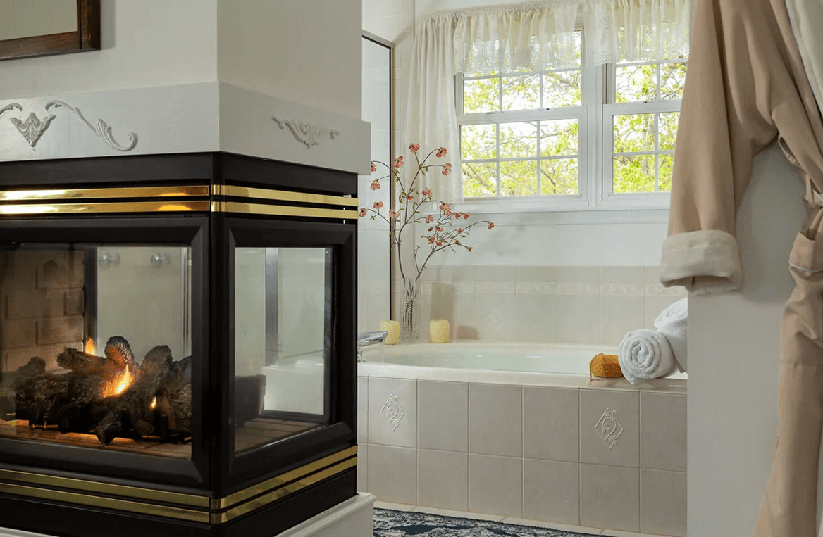 A serene bathroom featuring a glass-front fireplace, a spa tub, and natural light from windows. A serene bathroom featuring a glass-front fireplace, a spa tub, and natural light from windows.