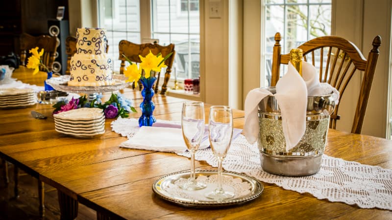 A beautifully set dining table with a decorated cake, champagne, glasses, and floral accents.