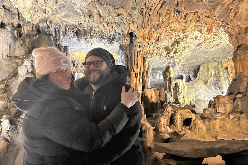 A couple smiles and embraces in a cave filled with impressive rock formations.