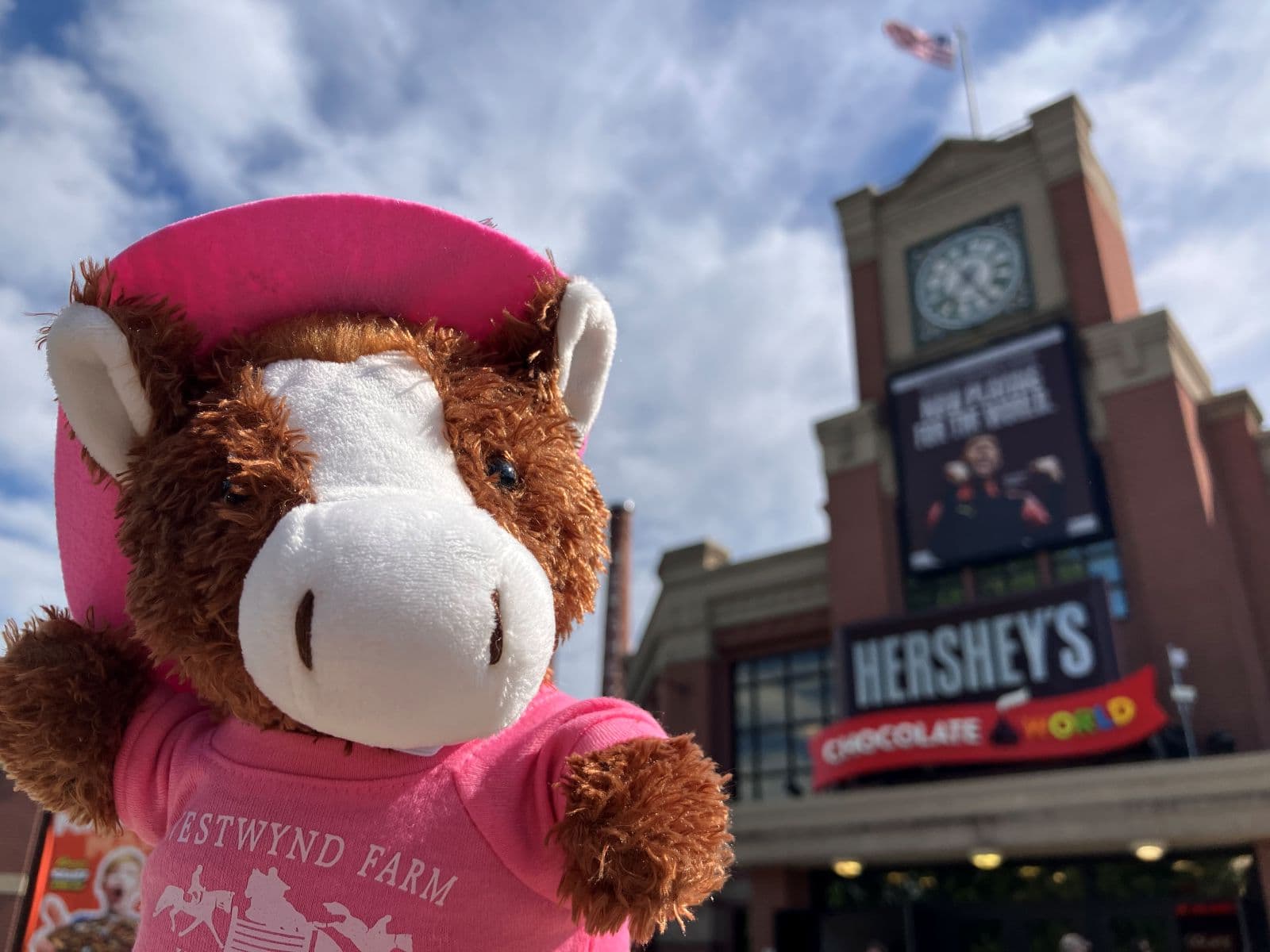 A stuffed cow wearing a pink hat stands in front of Hershey's Chocolate World.