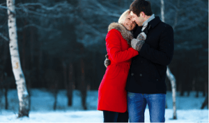 A couple embraces warmly in a snowy winter landscape.