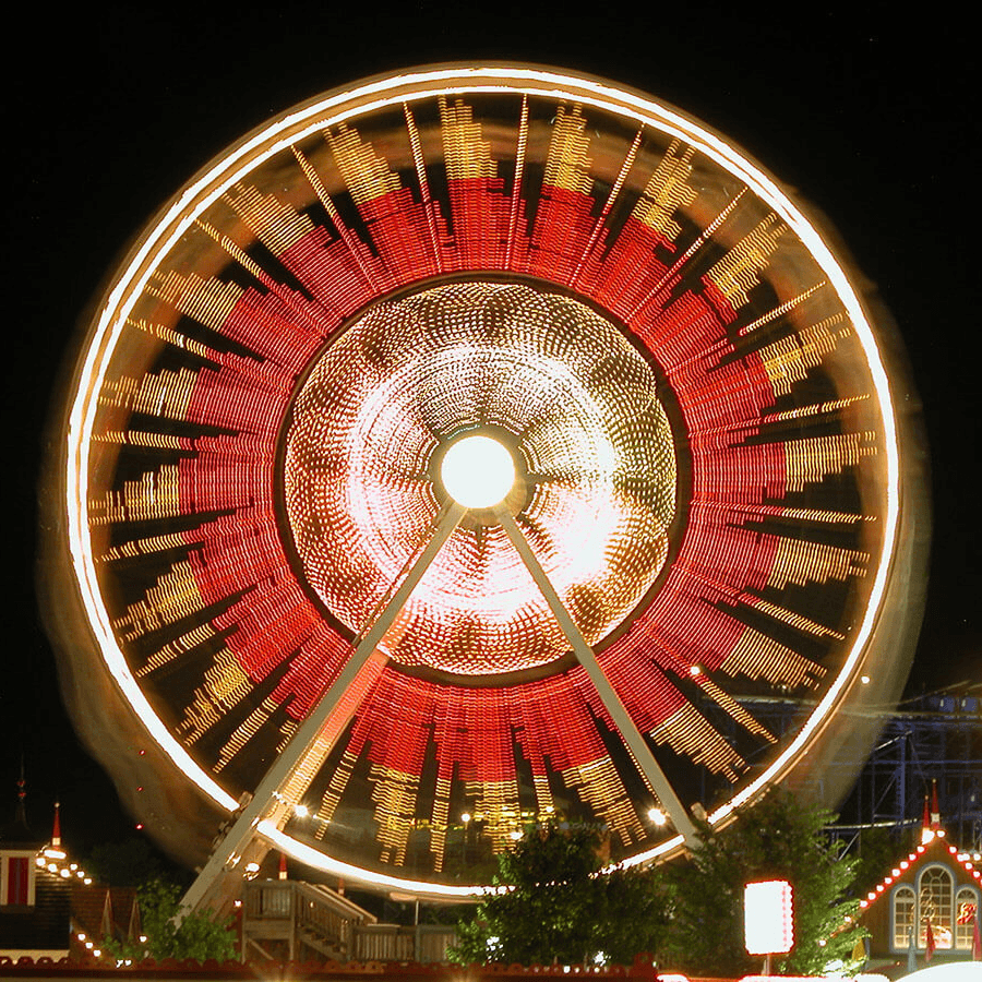 A brightly lit Ferris wheel spins at night, creating a vibrant display of lights.