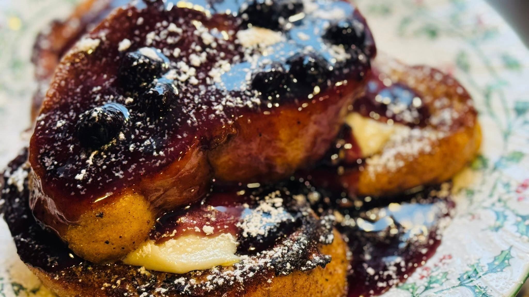 A plate of French toast topped with blueberry compote and powdered sugar.