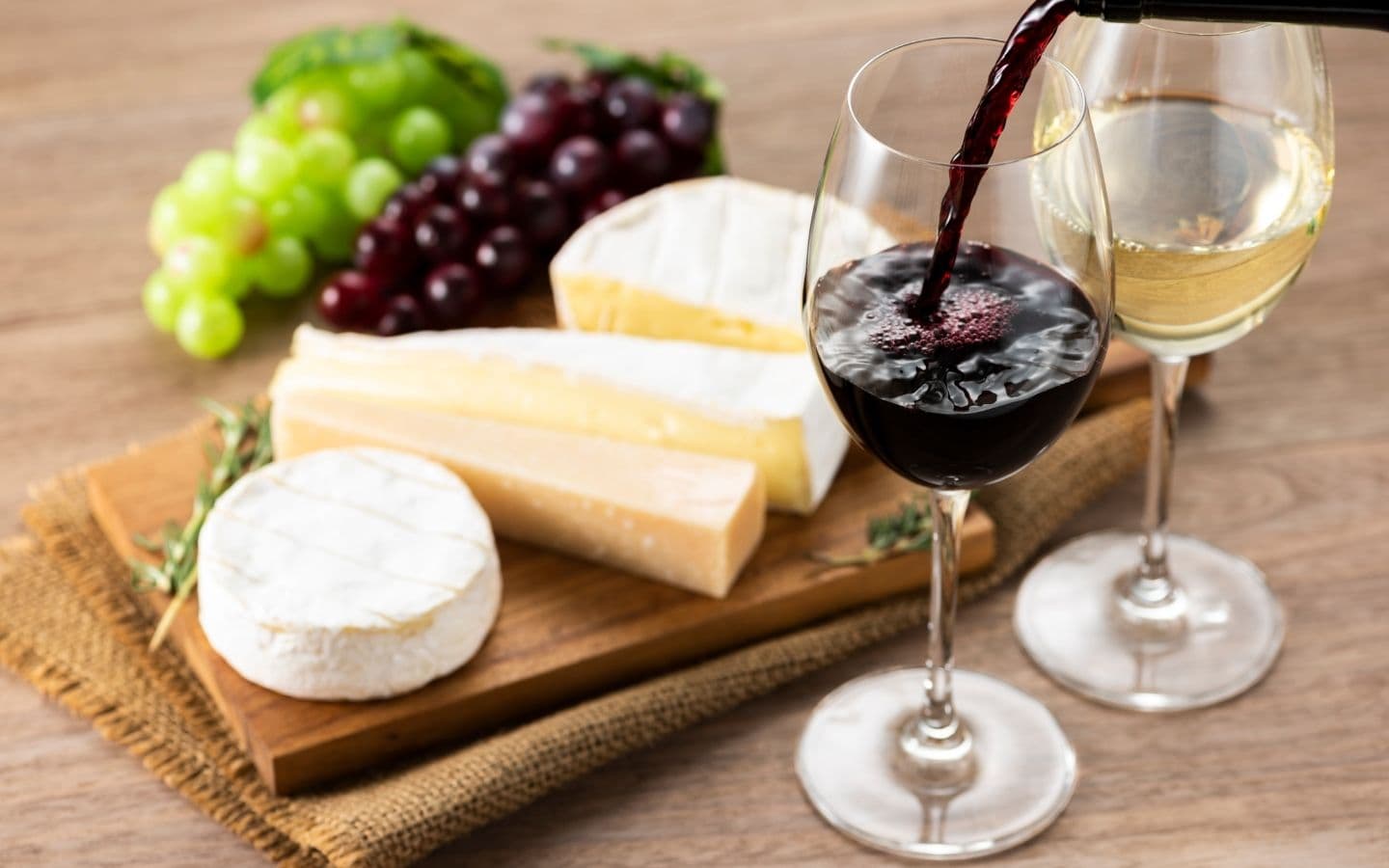 A wooden board with various cheeses, grapes, and two glasses of wine. A wooden board with various cheeses, grapes, and two glasses of wine.