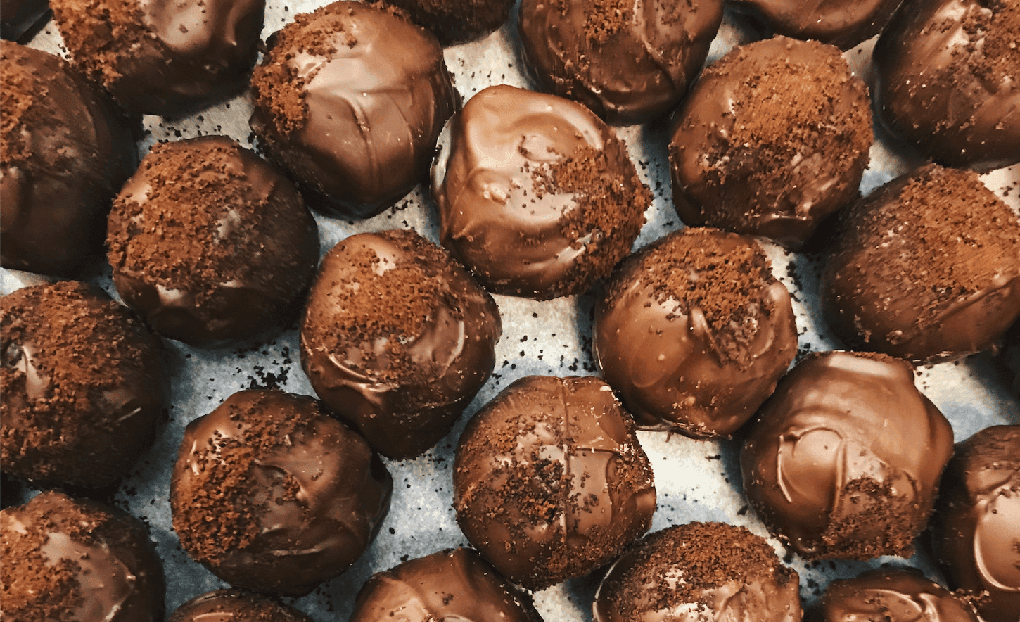 A close-up of chocolate-covered truffles sprinkled with cookie crumbs, arranged neatly on a tray.