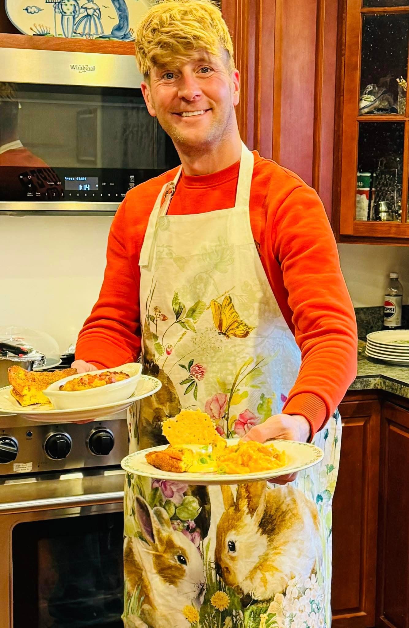 A person in an apron holds two plates of food in a kitchen.