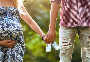 Couple holding hands and tiny baby shoes on babymoon