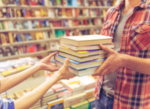 Man handing a stack of books to a cashier in a bookstore