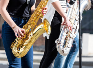 Two musicians playing saxophones outside