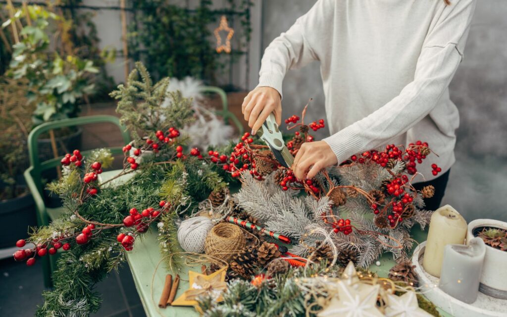 A woman creating Christmas wreaths with berries, string, evergreen boughs, etc.