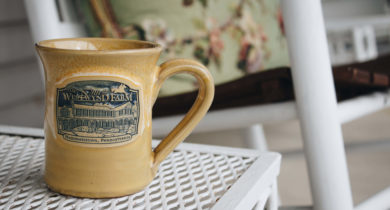 Close-up of a cup reading "The Inn at Westwynd Farm" which sits on small table on porch