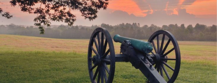 Civil war cannon in the grass amidst a sunset sky