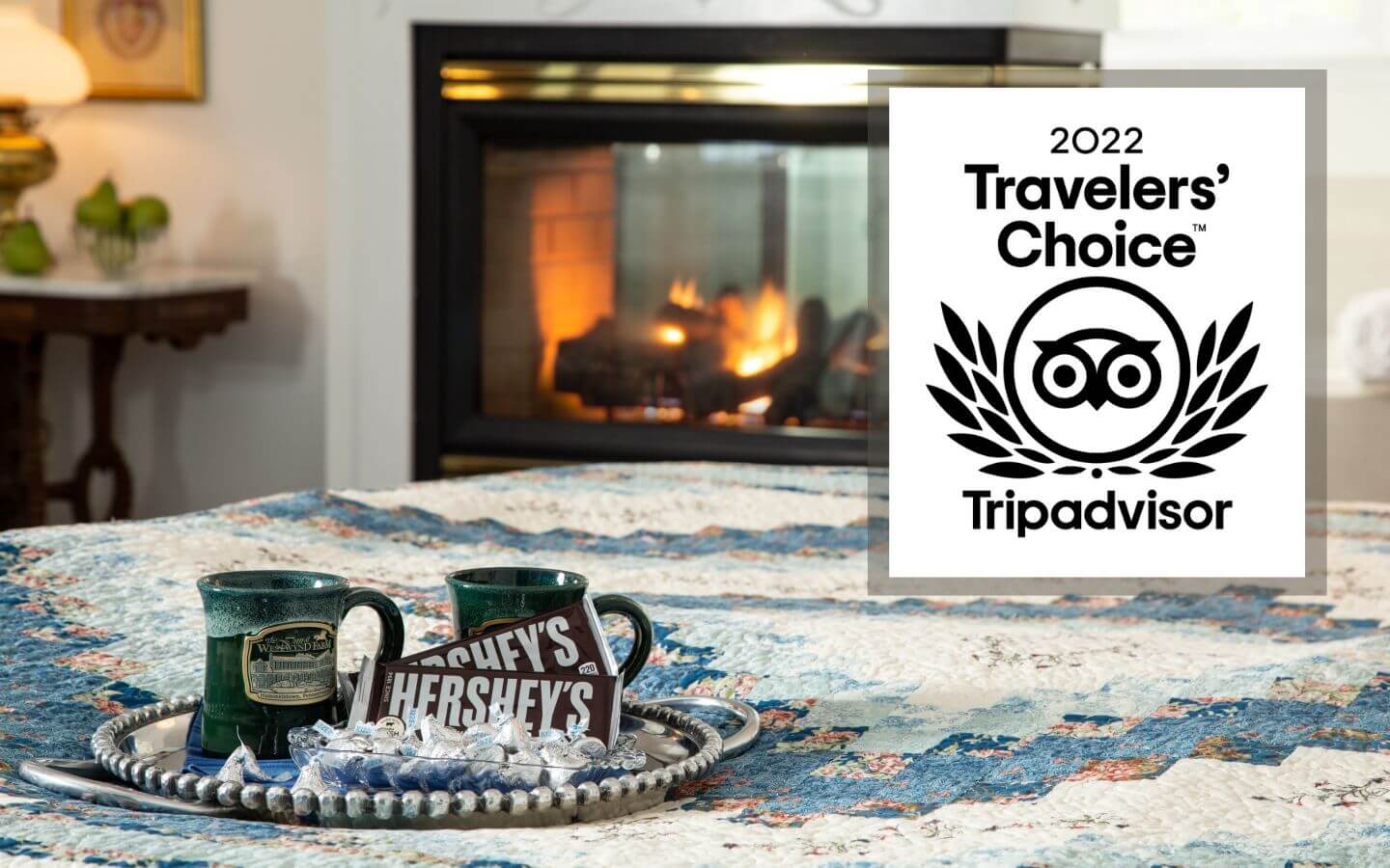 View of corner of bed, tray with mugs and chocolate, and a fireplace at the Inn at Westwynd Farm with 2022 TripAdvisor Travelers’ Choice Award